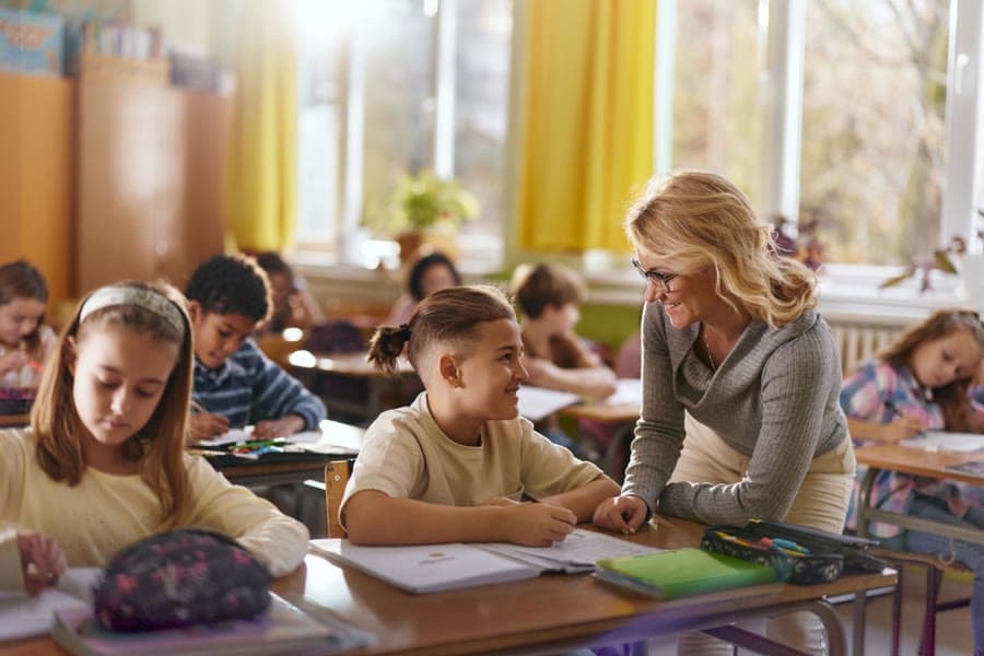 A Junior School teacher smiling with a student at their desk