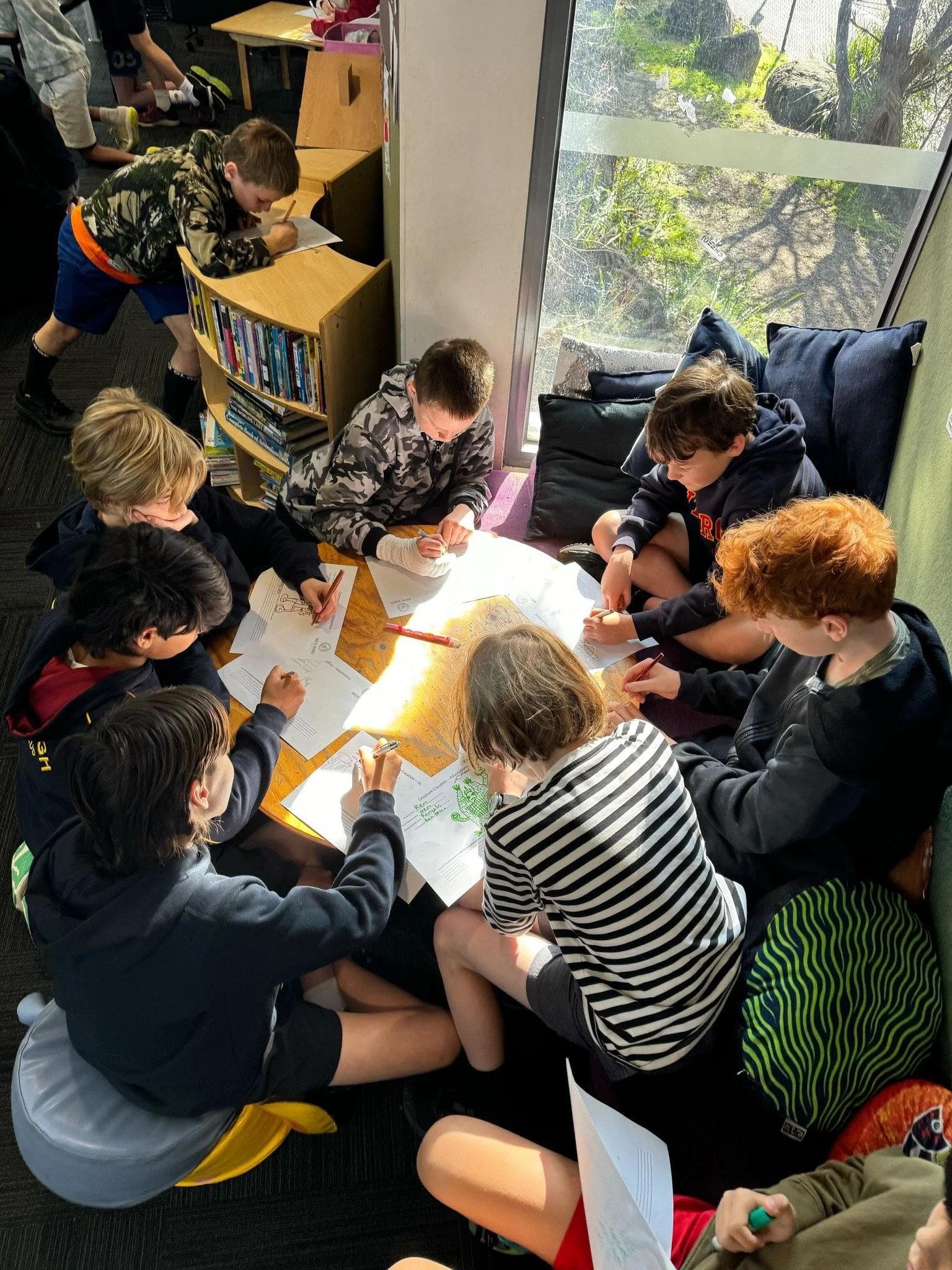 Junior school students gathered around a table reading and drawing together